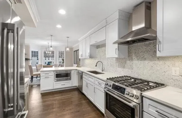 Modern white kitchen with stainless steel appliances, marble countertops, and hardwood floors