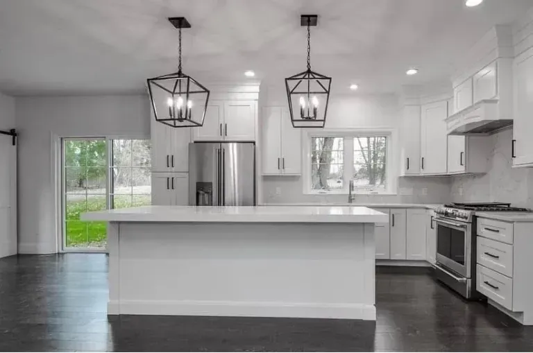 Bright modern white kitchen with island, pendant lights, stainless steel appliances, and dark wood floors