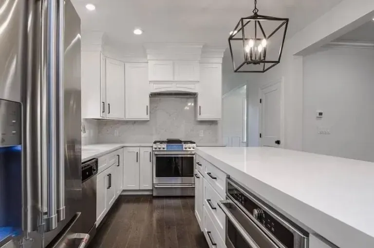 Modern white kitchen with stainless steel appliances, dark wood floors, and a large island countertop