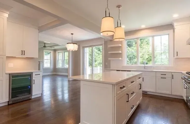 Bright open kitchen with white cabinets, dark wood floors, island, pendant lights, and large windows