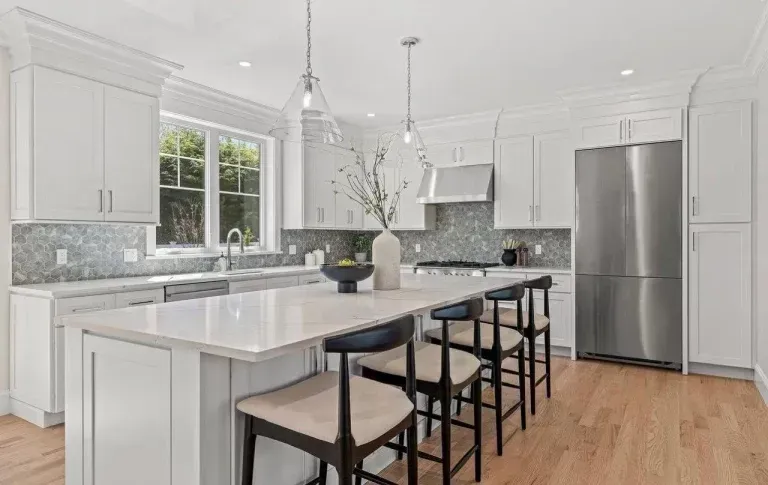 Bright modern kitchen with white cabinets, marble island, bar stools, and stainless steel refrigerator
