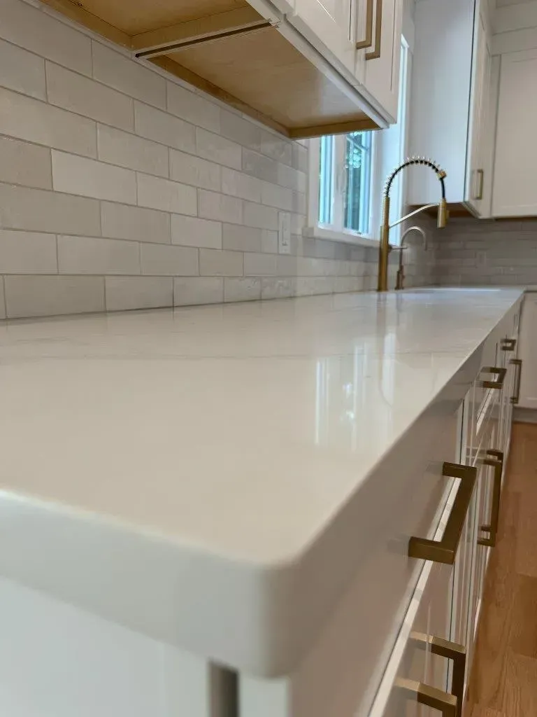 White kitchen countertop with subway tile backsplash and brass faucet by a window