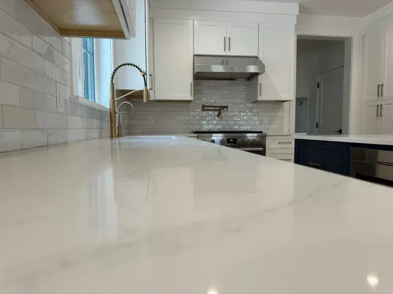 Bright modern kitchen with white cabinets, marble island, stainless range hood, and window over sink