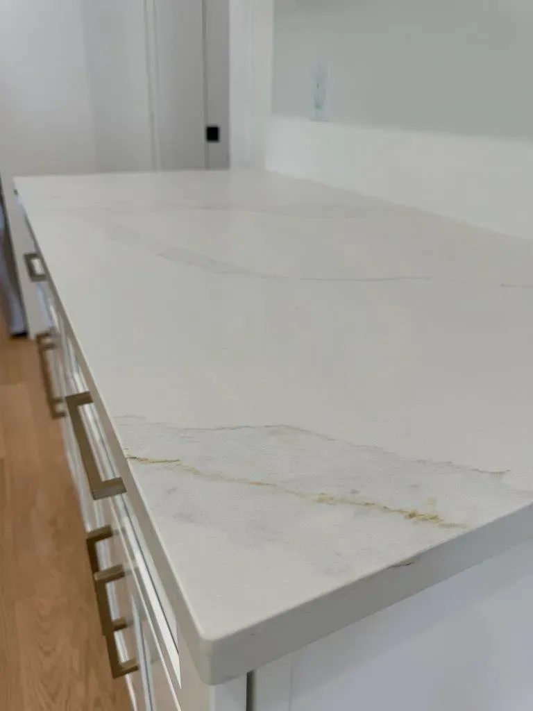 White kitchen countertop with subtle gray veining and wooden cabinet handles underneath