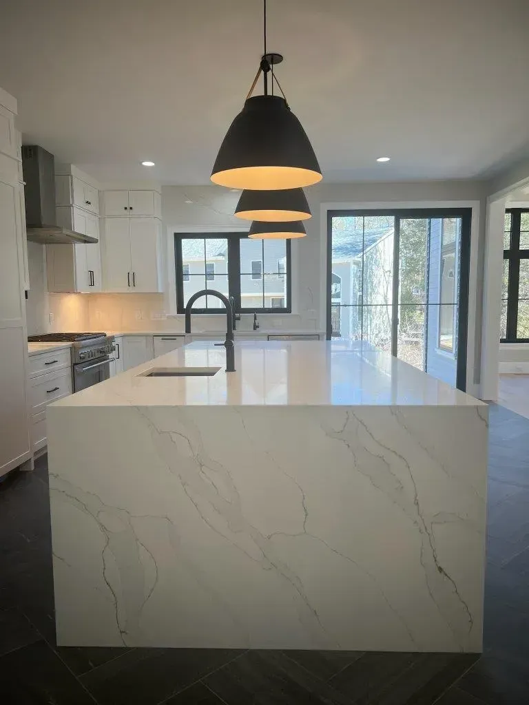 Modern kitchen with white marble island, black pendant light, and large windows overlooking trees