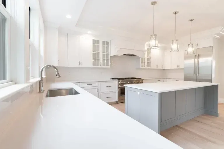 Bright white modern kitchen with a large island, stainless appliances, and pendant lights