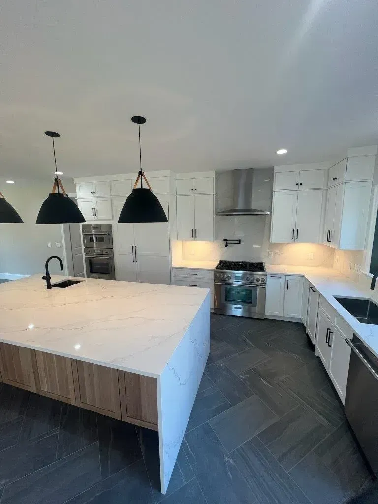 Modern white kitchen with large marble island, black pendant lights, and stainless steel appliances