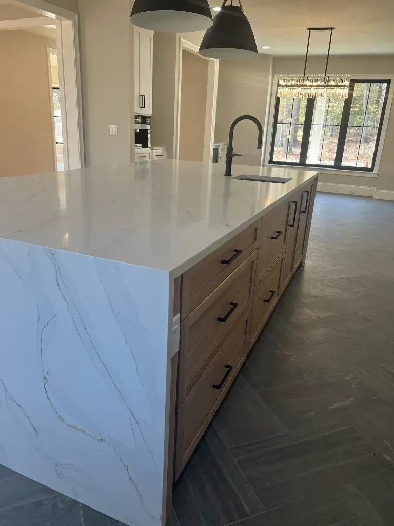Kitchen island with white marble countertop, wood drawers, and black pendant lights in a bright modern kitchen