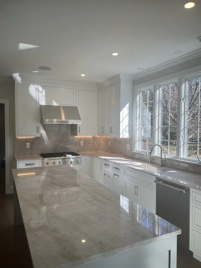 Bright modern kitchen with white cabinets, marble island, stainless steel appliances, and large windows