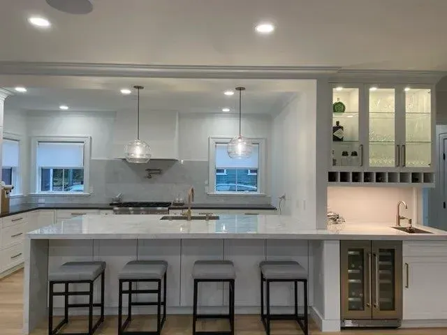 Modern white kitchen with island, pendant lights, barstools, and glass-front cabinets