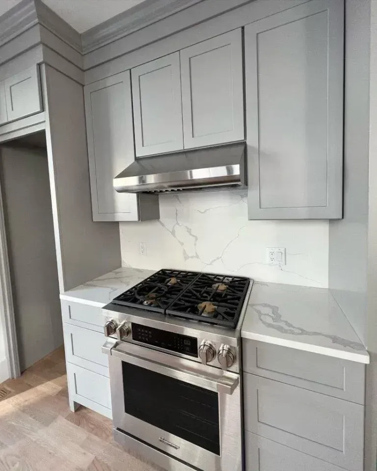 Modern kitchen with gray cabinets, marble-look countertops, and stainless steel gas range under a hood.