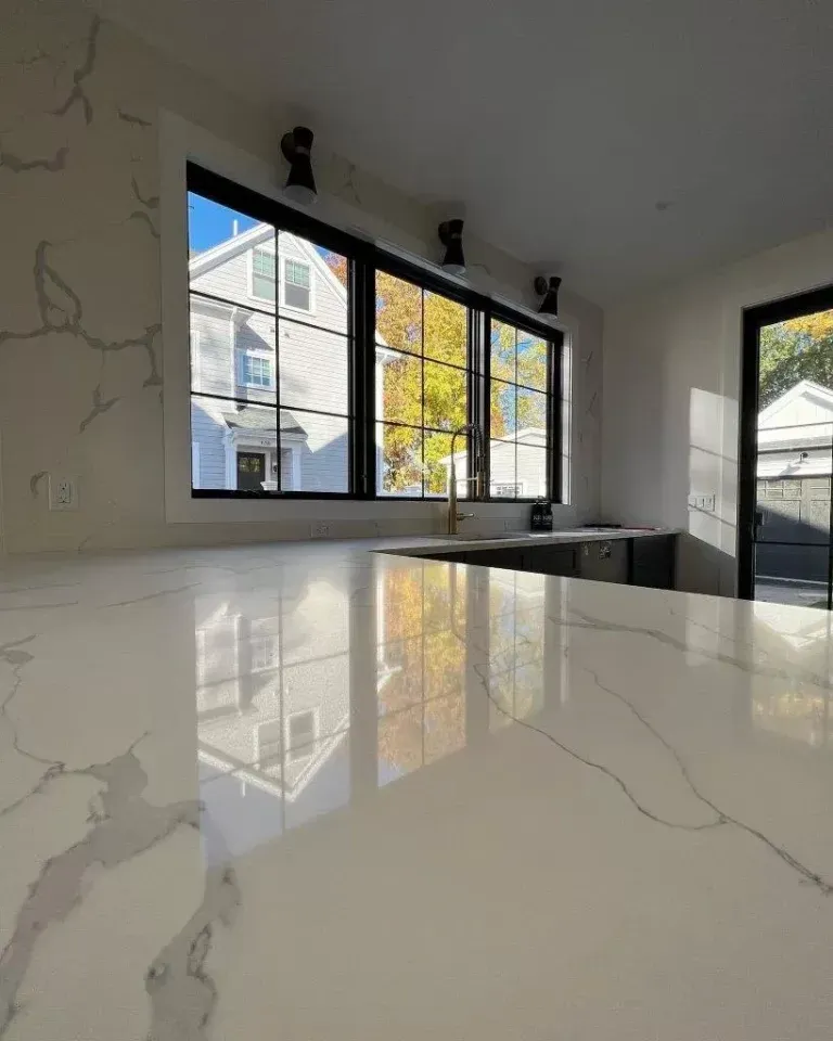 Modern kitchen with glossy white island, black-framed windows, and marble-look walls and counter
