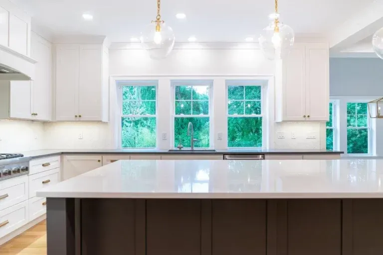 Bright white modern kitchen with a large island and windows overlooking green trees