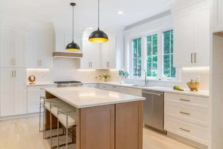 Bright modern white kitchen with island, pendant lights, and large window over the sink