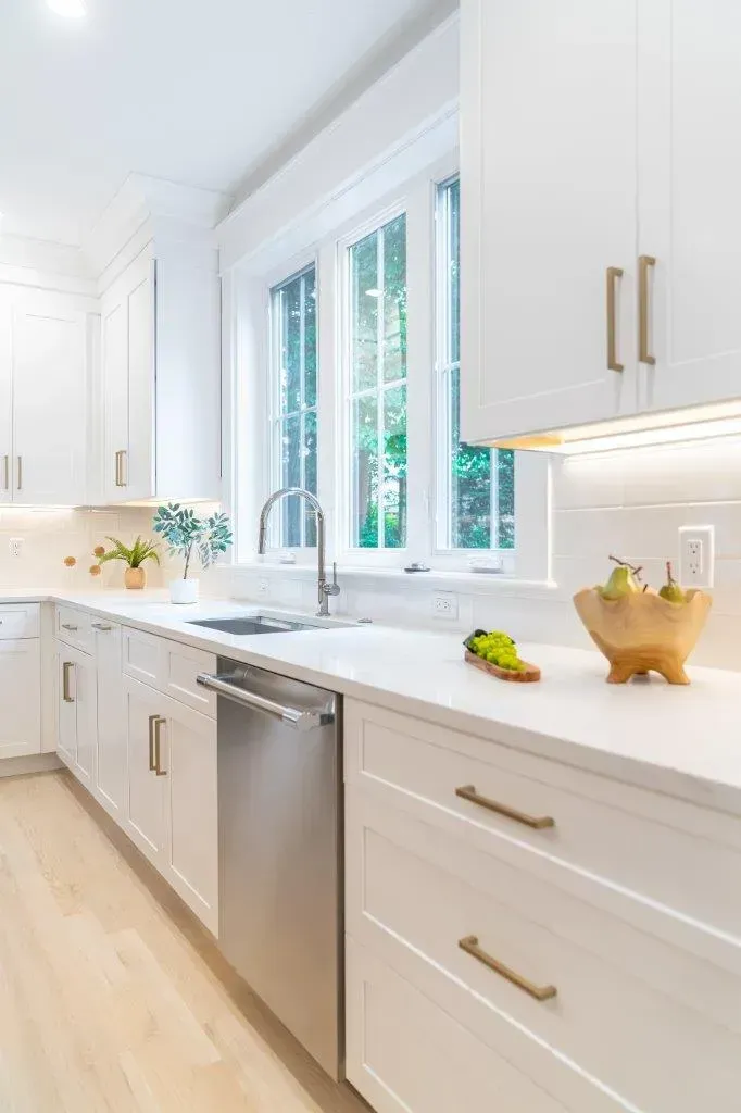 Bright white kitchen with stainless dishwasher, gold handles, and a bowl of bananas on the counter