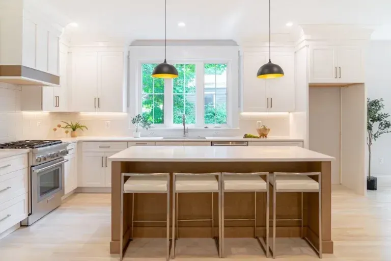 Bright modern kitchen with white cabinets, island, pendant lights, and large window