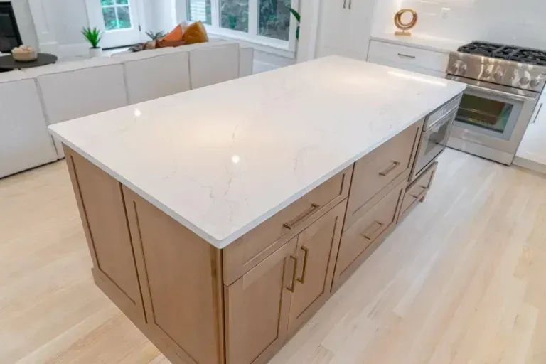 Modern kitchen island with white quartz countertop and light wood cabinets on a bright floor