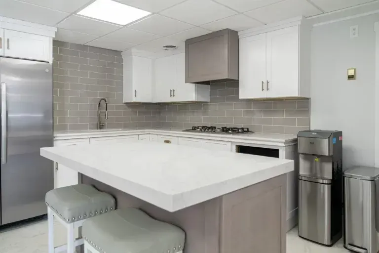 Modern kitchen with white island, stools, stainless fridge, and light gray cabinets
