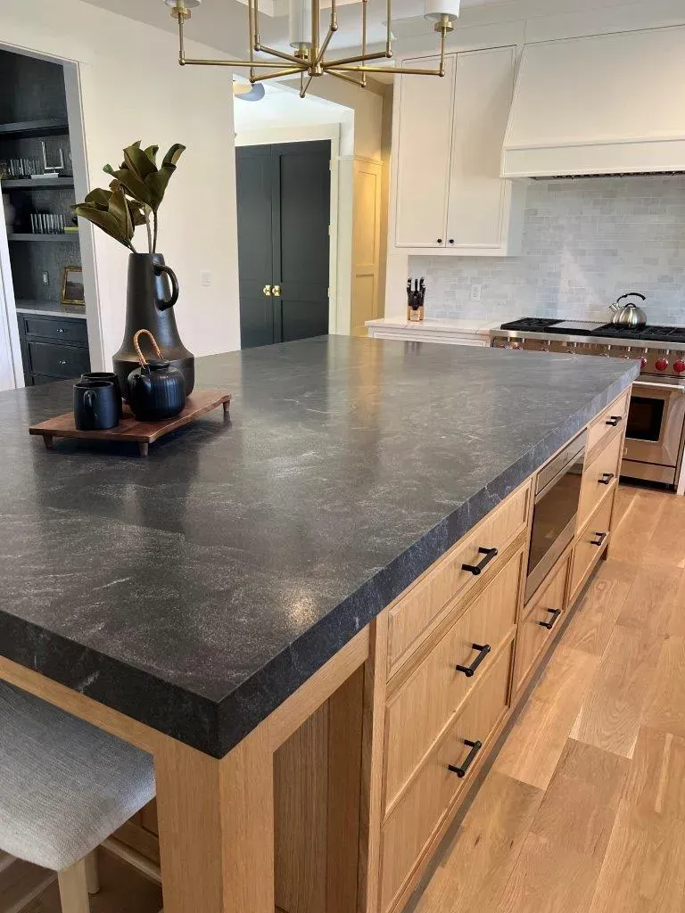 Modern kitchen with black countertop, wooden island drawers, and decorative vase on a tray