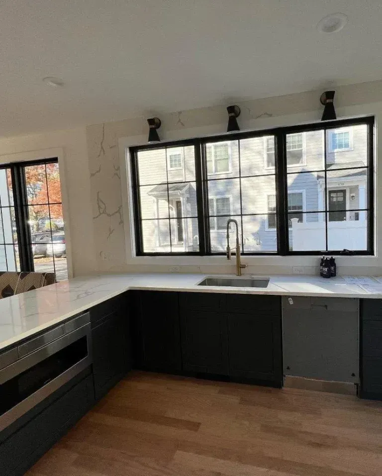Modern kitchen with black-framed windows, white countertops, dark lower cabinets, and wood flooring.