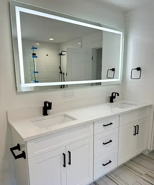 Modern white bathroom vanity with double sinks, black faucets, and a large backlit mirror.