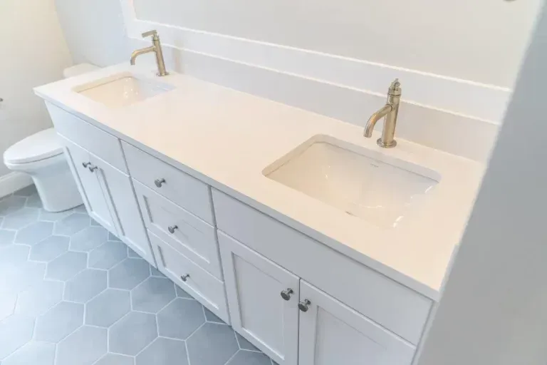 Double bathroom vanity with white countertops, two sinks, brass faucets, and gray hex tile floor