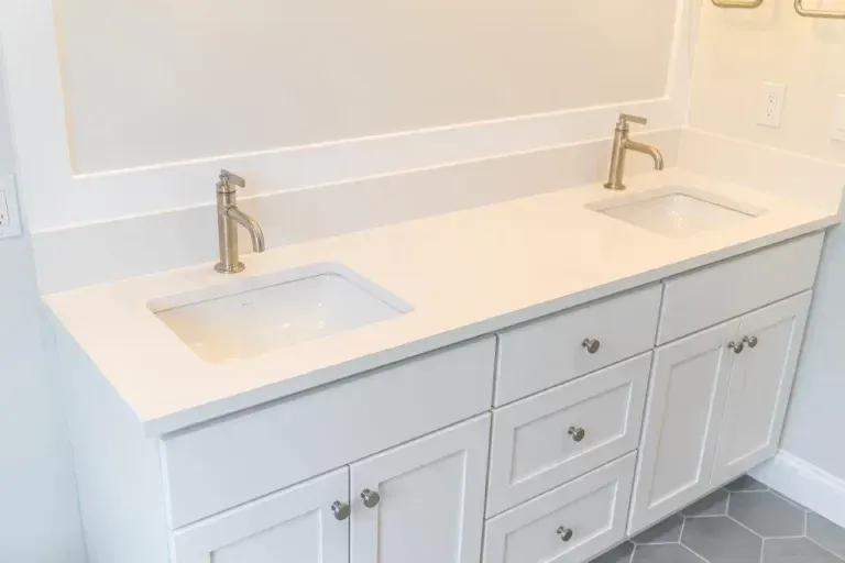 White double-sink bathroom vanity with brass faucets and cabinet drawers under a wall mirror