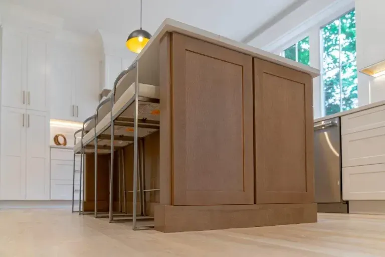 Modern kitchen with a large wooden island, pendant lights, and white cabinets by a window
