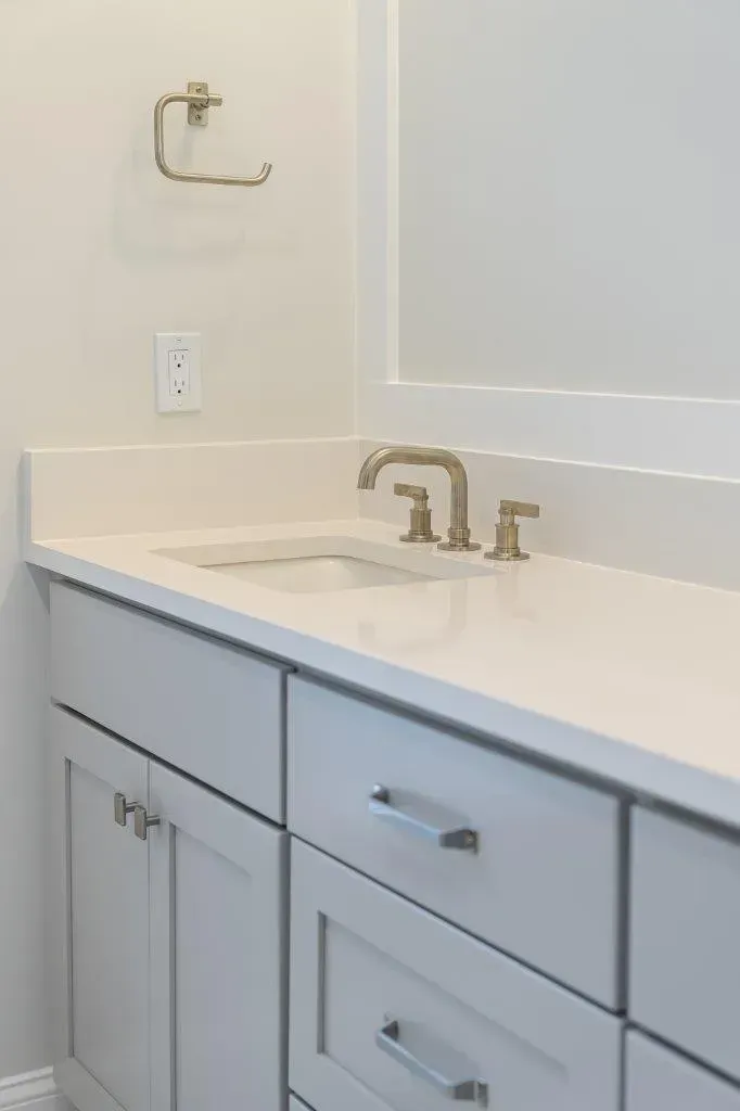 Modern white bathroom vanity with sink, gold faucet, and mirror wall cabinet.