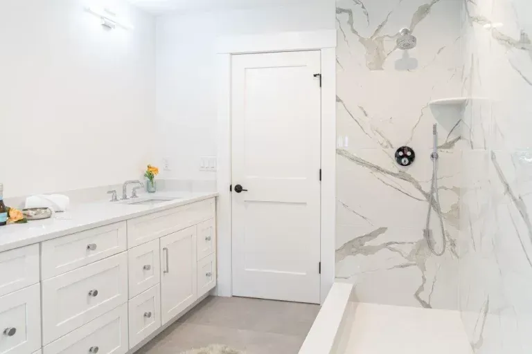 Modern white bathroom with double vanity and marble shower wall inside a bright interior