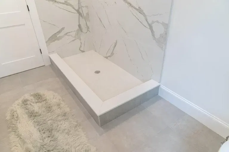 Bathroom shower nook with white tiled step, marble wall, and small drain cover