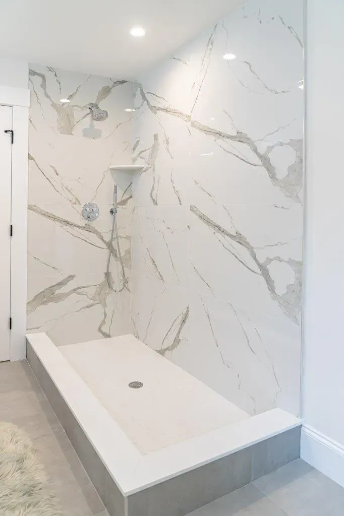 White marble-tiled walk-in shower with a built-in bench and a single showerhead.