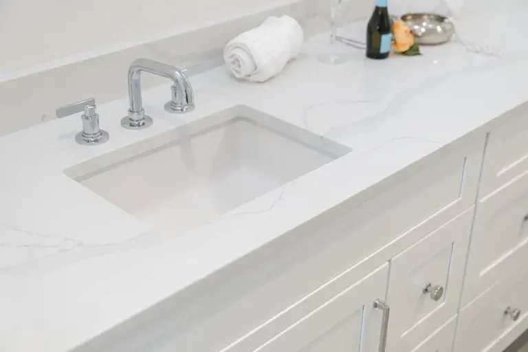 White bathroom vanity with sink, chrome faucet, and a few toiletries on the countertop.