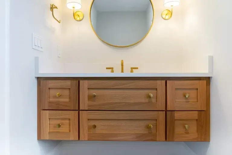 Modern bathroom vanity with wooden drawers, gold fixtures, and round mirror on a white wall