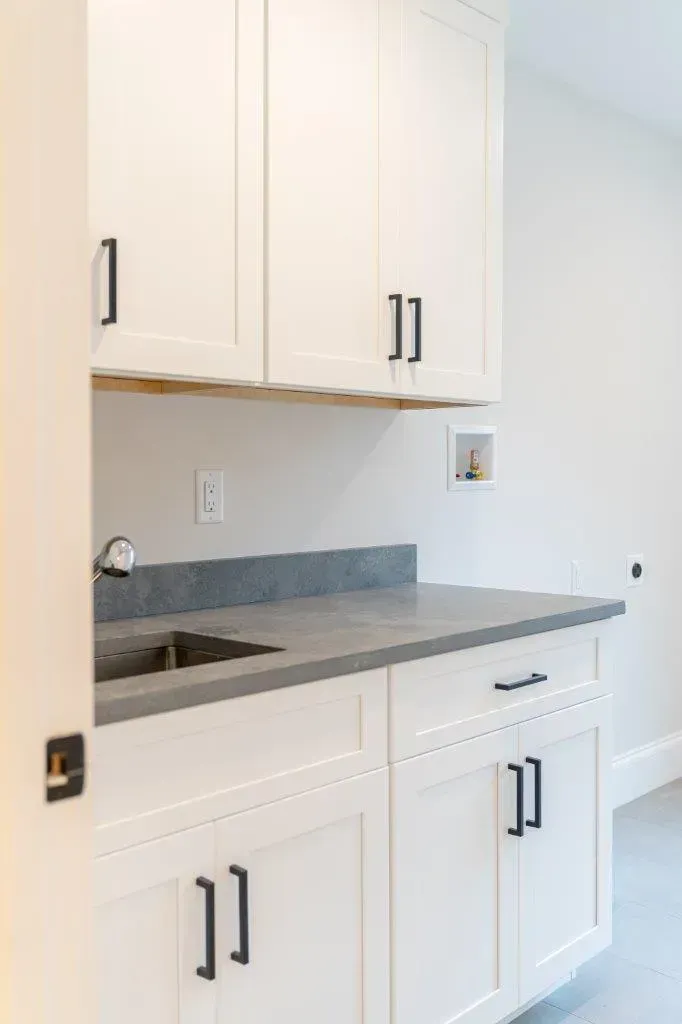 White kitchen cabinets and gray countertop with sink, in a bright empty room