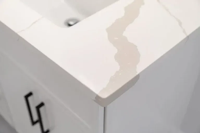 White corner cabinet with water stains on the top surface and a black handle on the side