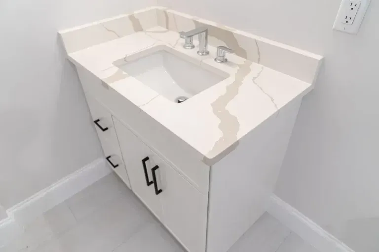 White bathroom vanity with built-in sink, marble countertop, and black handles against a light wall