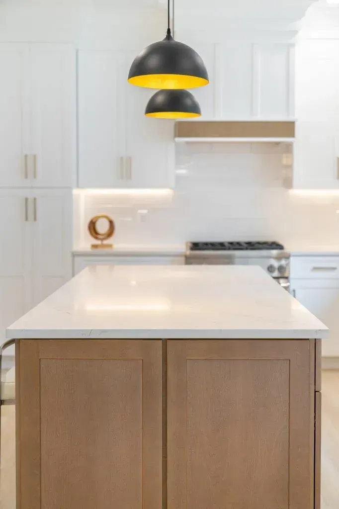 Modern white kitchen with wood island, black pendant light, and stainless steel stove