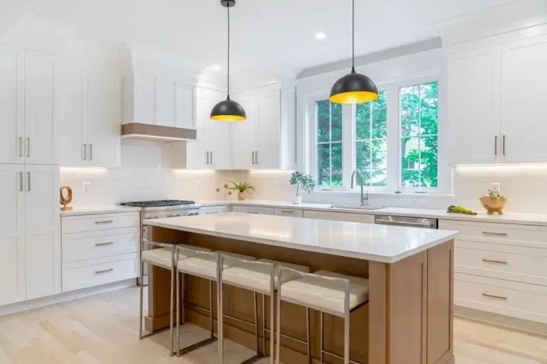 Bright modern white kitchen with island, stools, pendant lights, and large window