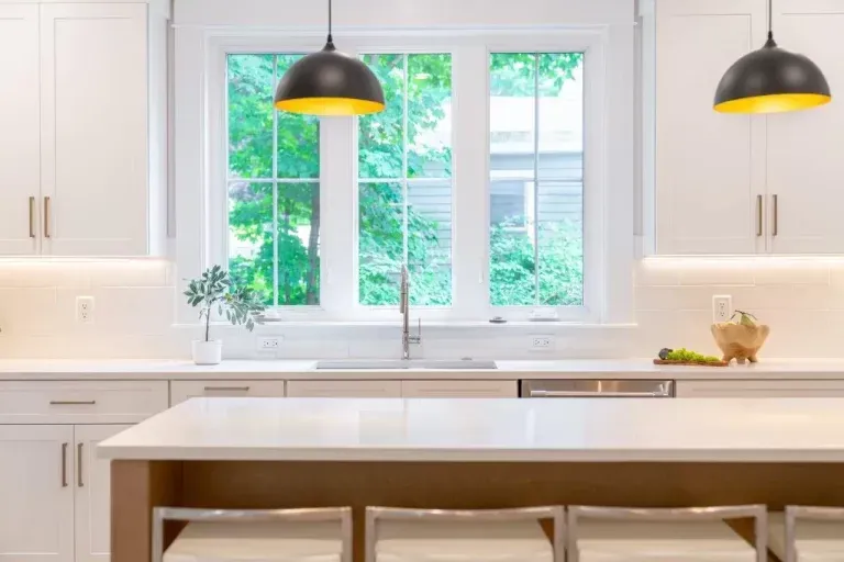Bright white kitchen with a large window, black pendant lights, and a countertop island.
