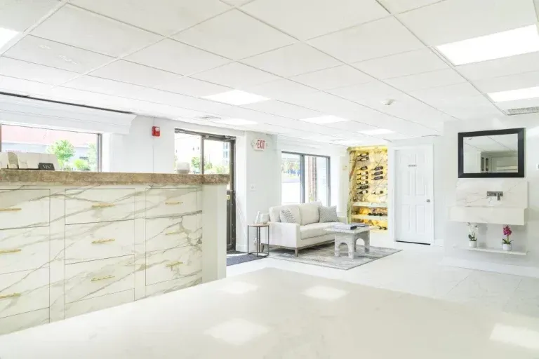 Bright white modern lobby with marble reception desk, seating area, and glass doors under a drop ceiling