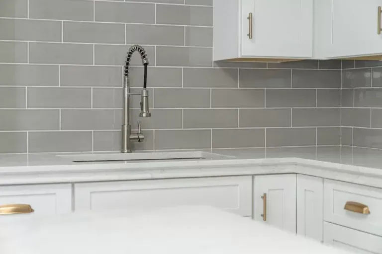 Modern white kitchen with gray subway tile backsplash and stainless gooseneck faucet over sink