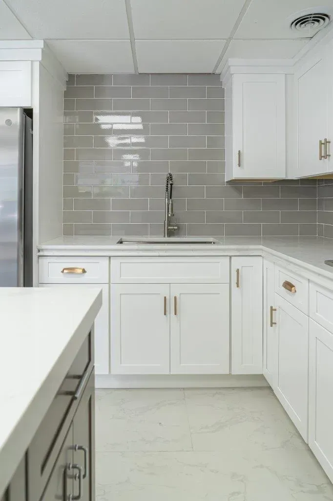 Bright white kitchen with gray subway tile backsplash, white cabinets, and stainless faucet at the sink.