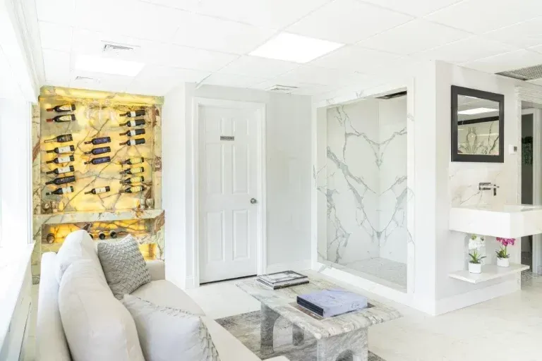 Bright modern living room with white sofa, marble fireplace, gold wine rack, and glass coffee table