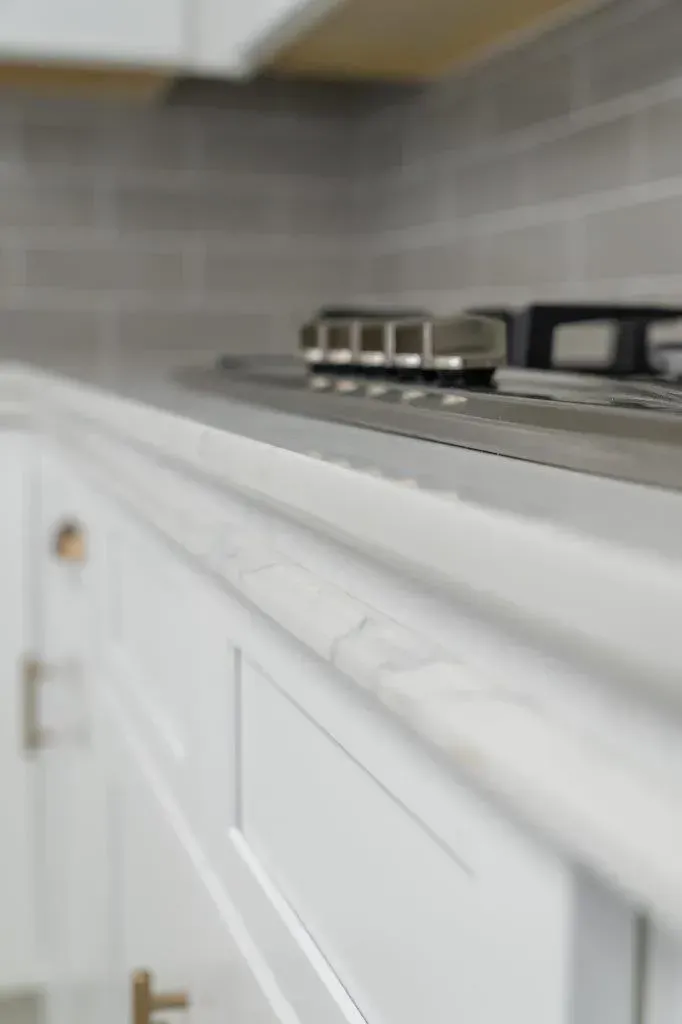 Small model train on a gray rail atop a white cabinet in a tiled kitchen