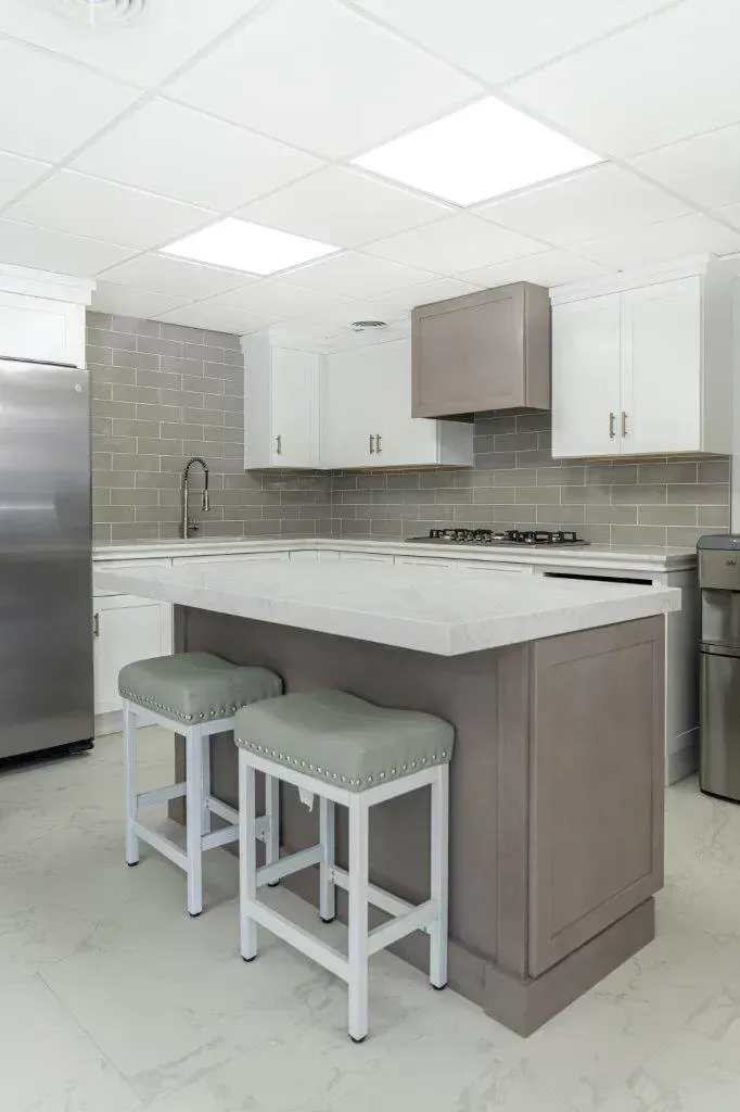 Modern kitchen with white cabinets, gray island, and two stools under bright ceiling lights