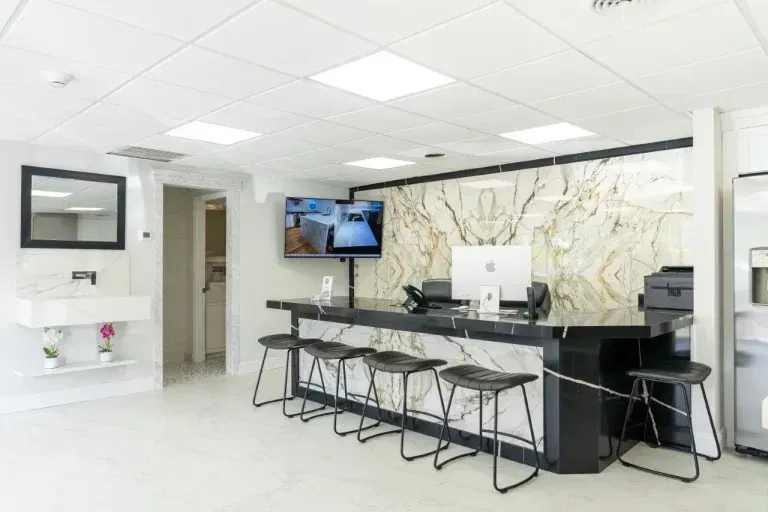 Bright modern reception desk with white marble wall, computer monitors, and black wire chairs