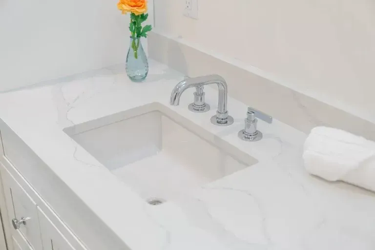 White marble bathroom vanity with built-in sink, chrome faucet, towel, and vase with orange flowers