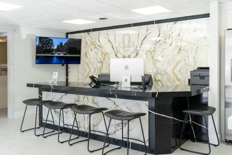 Modern office reception desk with marble wall, stools, and a wall-mounted TV