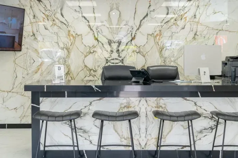 Modern reception desk with three stools and a white marble-patterned wall backdrop